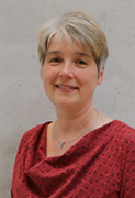 Porträt von Dr. Andrea Eschemann, Beratung und Verkauf für die Postleitzahlengebiete 35, 60 (nur Goethe-Universität Frankfurt), 61 und 64. Sie trägt eine rote gemusterte Bluse und hat kurze, grau-blonde Haare. Der Hintergrund ist eine helle Betonwand.